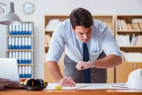 Mężczyzna w biurze sprawdza zegarek, martwiąc się o nieobecność w pracy.