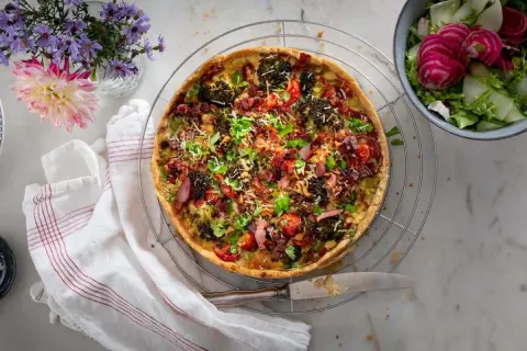 En gyllene quiche lorraine med broccoli, bacon och tomater, serverad med en fräsch sallad.