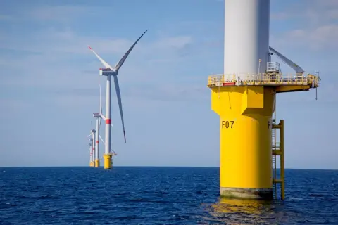 Wielkie turbiny wiatrowe na Bałtyku, symbolizujące **baltic power**, generują czystą energię na tle błękitnego nieba.