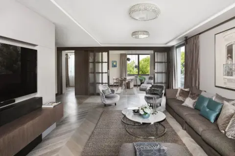 Elegancki salon z kanapą, fotelami i stolikiem kawowym. W tle widać jadalnię i okno z widokiem na zieleń. Całość emanuje wyrafinowanym, **włoskim stylem**.