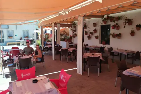 Pareja sonriente en la terraza de "La Chumbera Las Negras", un restaurante con mesas al aire libre y macetas de flores.