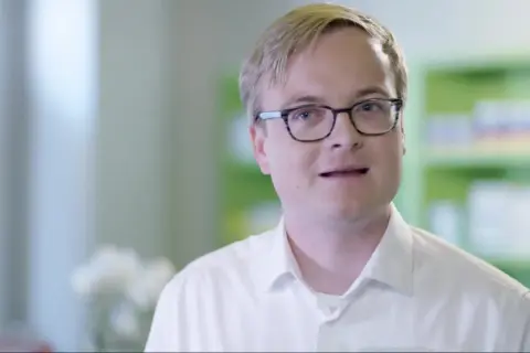 Ein Mann mit Brille in einem weißen Hemd spricht. Er erklärt, dass es erleada eine Chemotherapie ist.
