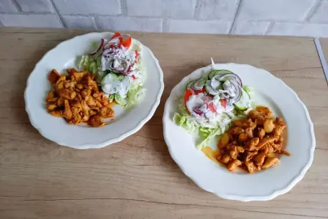 Dwa talerze z kurczakiem w przyprawach i sałatką z pomidorów, ogórków i cebuli. Tak wygląda pyszna shoarma co to za danie!