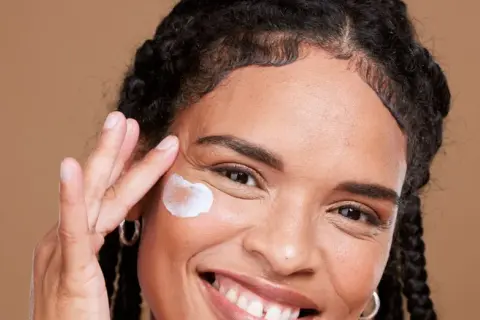 Lächelnde Frau trägt eine Creme auf, die für die vitamin c haut gedacht ist.