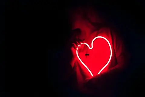 Een persoon houdt een gloeiend rood neonhart vast. Dit is wat ontgroend liefde kan voelen: warm, helder en vol passie.