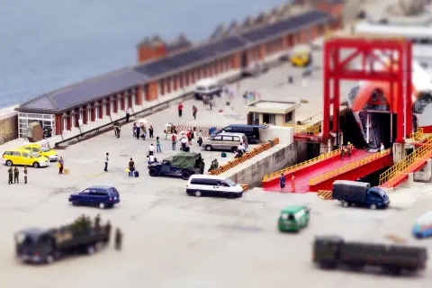 Scène de port avec des véhicules et des personnes, effet tilt shift donnant une impression de maquette.