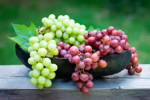 Grappoli di uva verde e rossa in una ciotola scura, su un tavolo di legno. Ricorda che l'uva è lassativa!