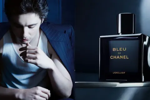 Młody mężczyzna w garniturze i podkoszulku, obok flakonik perfum BLEU DE CHANEL L'EXCLUSIF.