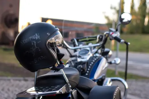 Czarny kask motocyklowy z napisem "Scorpion" i grafiką skorpiona, oparty o siedzenie choppera.