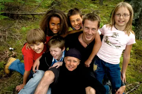 En grupp glada barn och en vuxen njuter av en dag i skogen. De ser ut som riktiga ola wild kids, redo för äventyr.
