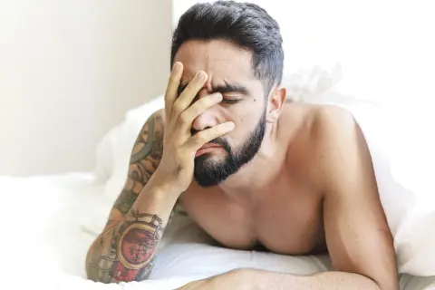 Mężczyzna z tatuażami na ramieniu, z ręką na twarzy, zastanawia się, w jakim wieku spada popęd seksualny u mężczyzn.