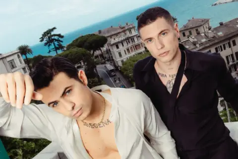 Benji e Fede posano con un panorama mozzafiato alle loro spalle, tra case colorate e il blu del mare.