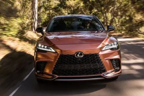Miedziany Lexus RX 450h pędzi leśną drogą, światła LED rozświetlają trasę.