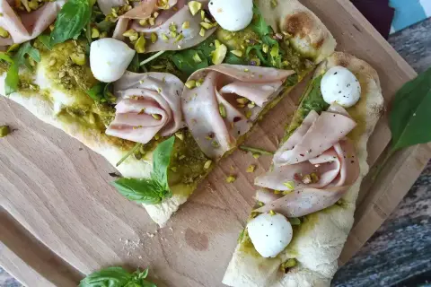 En läcker pinsa pesto med mortadella, mozzarella, pistagenötter och färsk basilika på en träskärbräda.