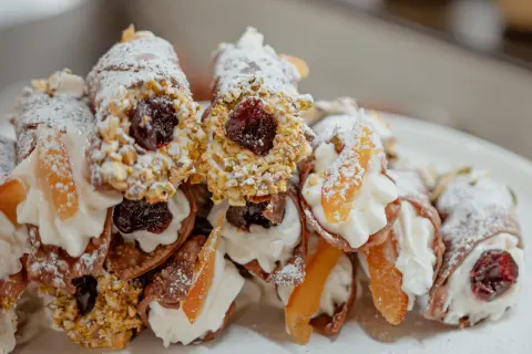 Cannoli garnis avec une généreuse crème de ricotta, des pistaches concassées, des cerises confites et des fruits confits. Saupoudrés de sucre glace.