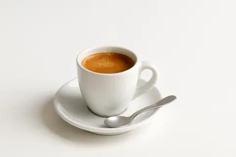 Tazzina di caffè espresso su piattino bianco con cucchiaino. Un piacere quotidiano, ma attenzione al caffè e colesterolo.