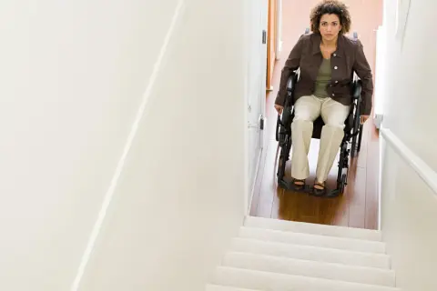 Donna in carrozzina guarda verso l'alto, pronta per il trasporto disabile su per le scale.
