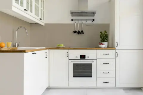 Moderne weiße Küche mit Holzoberflächen und grauen Fliesen. Ein Herd, ein Spülbecken und Obst sind zu sehen. Die Idee, die alten Fliesen zu streichen, passt gut zu diesem Stil.