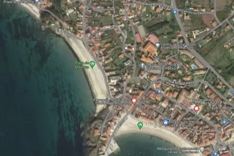 Vista aérea de la **playa de Madorra**, con el mar turquesa y la arena dorada. Se aprecian edificios y calles cercanas.