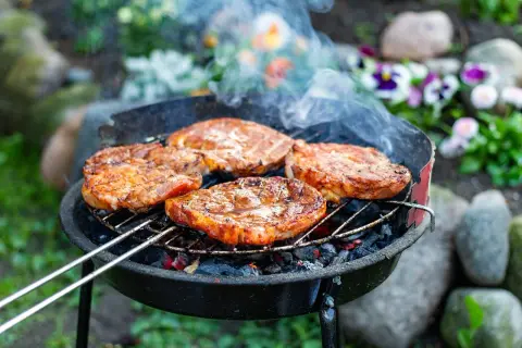 Saftige Steaks brutzeln auf dem Grill. Tolle Grill Tipps für ein perfektes Ergebnis. Rauch steigt auf, Blumen blühen im Hintergrund.