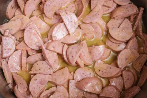 Scheiben von Lyoner Wurst in einer gelben, würzigen Soße, bereit für einen herzhaften Wurstsalat.