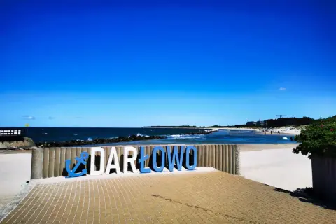 Napis "DARŁOWO" na plaży, zapraszający do odkrywania atrakcji nad Bałtykiem.