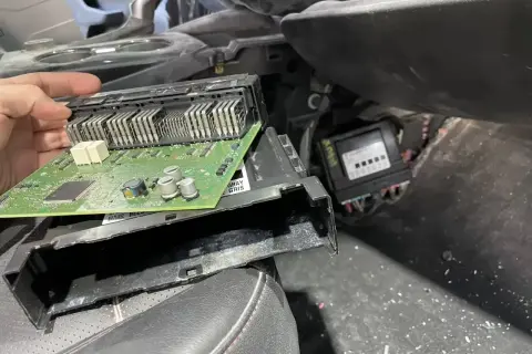 Ręka trzyma moduł elektroniczny z zieloną płytką drukowaną, prawdopodobnie związany z błędem dtc u0140 opel. Obok widoczny inny moduł.