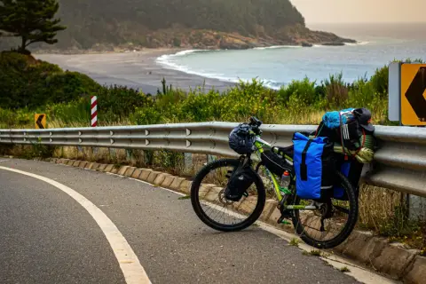 Rower gotowy do bike packingu, obładowany bagażami, stoi przy drodze z widokiem na ocean i plażę.