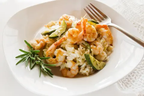 Cremiges Risotto mit Garnelen und Zucchini, garniert mit Rosmarin. Ein köstliches Gericht, das Lust auf mehr macht.