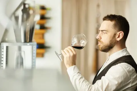 Mężczyzna, degustator win, wącha kieliszek czerwonego wina, oceniając jego aromat.