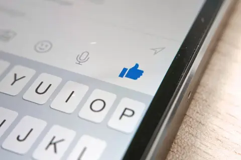 Kciuk w górę na ekranie telefonu, pokazujący, jak działa aktywność na Messengerze. Klawiatura i ikony czatu.