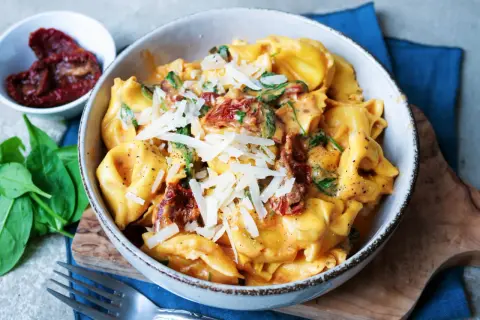 Cremige Tortellini mit Spinat und getrockneten Tomaten, bestreut mit Parmesan. Ein köstliches Gericht, das Lust auf mehr Tortellini Rezepte macht.