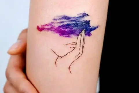 Tatuaje de una mano sosteniendo una nube morada y azul, simbolizando la superación de la ansiedad.