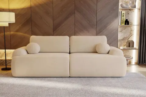 Eine cremefarbene Couch mit runden Kissen, die zum Entspannen einlädt. Sie steht vor einer Holzwand und einem Regal mit Büchern und Deko.