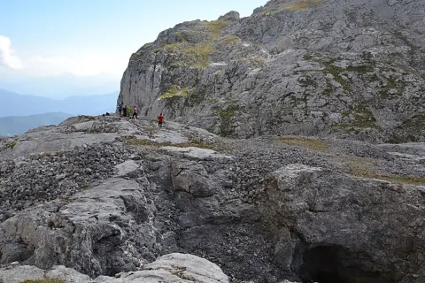 Senderismo en la vega de Liordes, un paisaje rocoso con un grupo de personas observando un abismo.