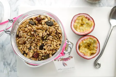 Glas mit selbstgemachtem Granola, Kürbiskernen und Trockenfrüchten. Daneben zwei Passionsfrüchte und ein Löffel.