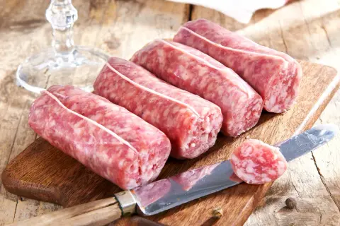 Frische Salsiccia auf Holzbrett, bereit, in Wasser zu kochen. Ein Messer liegt daneben.