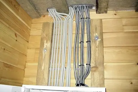 Instalacja elektryczna w drewnianej ścianie. Rury ochronne z przewodami wychodzą z sufitu. Czy drewno przewodzi prąd? Bezpieczeństwo przede wszystkim!