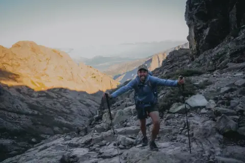 Un randonneur souriant sur un sentier rocheux, bâtons en main. Il semble se demander quel est le gr le plus difficile.