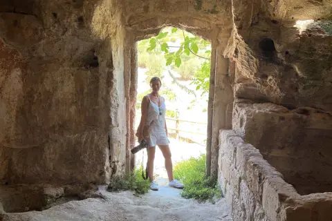 Una donna in abito bianco, con una macchina fotografica in mano, esplora antiche rovine. Un momento di travel photography.