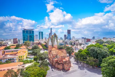 Piękna pogoda w Ho Chi Minh: katedra Notre Dame i nowoczesne wieżowce na tle błękitnego nieba z chmurami.