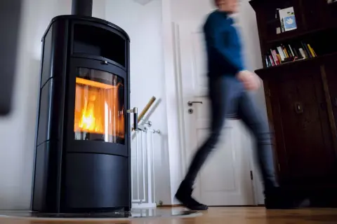 Ein Mann eilt an einer brennenden Holzheizung vorbei. Angesichts des möglichen Holzheizung Verbots 2030, wird diese Heizform bald Geschichte sein.