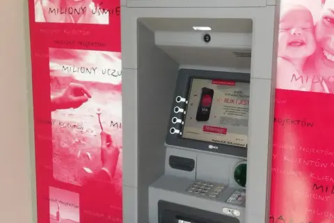 Bankomat Millennium z hasłem "miliony uśmiechów". Obok reklamy z uśmiechniętymi dziećmi i hasłem "miliony uczuć".