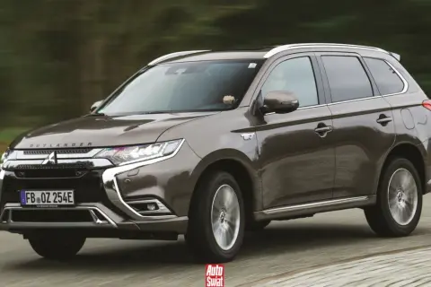 Brązowy Mitsubishi Outlander PHEV w ruchu, z widocznym napisem "OUTLANDER" na masce i emblematem "EV" na błotniku.