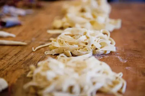 Frische Pasta, bereit für ein köstliches Pasta fresca Rezept, liegt auf einem Holztisch.