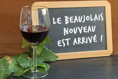 Kieliszek czerwonego wina i tablica z napisem "Le Beaujolais Nouveau est arrivé!" – to znak, że nadszedł czas na święto młodego wina.