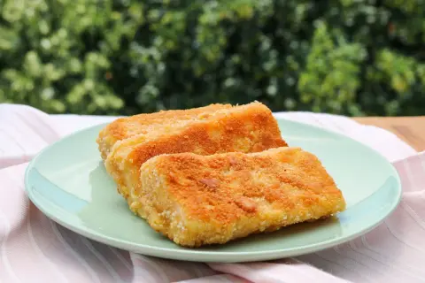 Zwei goldbraun gebackene Emmentaler-Schnitzel auf einem hellgrünen Teller, serviert mit einem rosafarbenen Tuch.
