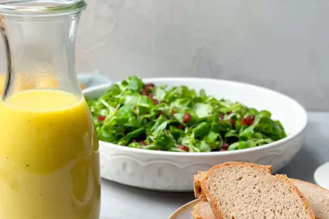 Ein Glas mit gelbem Dressing steht neben einem Salat und Brot. Perfekt für ein Kartoffel Dressing!