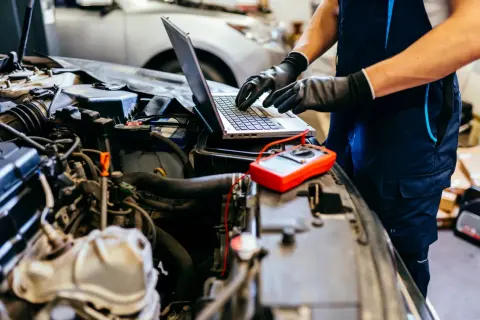 Mechanik diagnozuje problem z silnikiem 4t, który się dusi po dodaniu gazu. Na laptopie analizuje dane, obok leży multimetr.