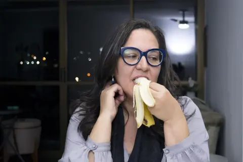 Kobieta w okularach je banana na noc, ciesząc się smakiem.